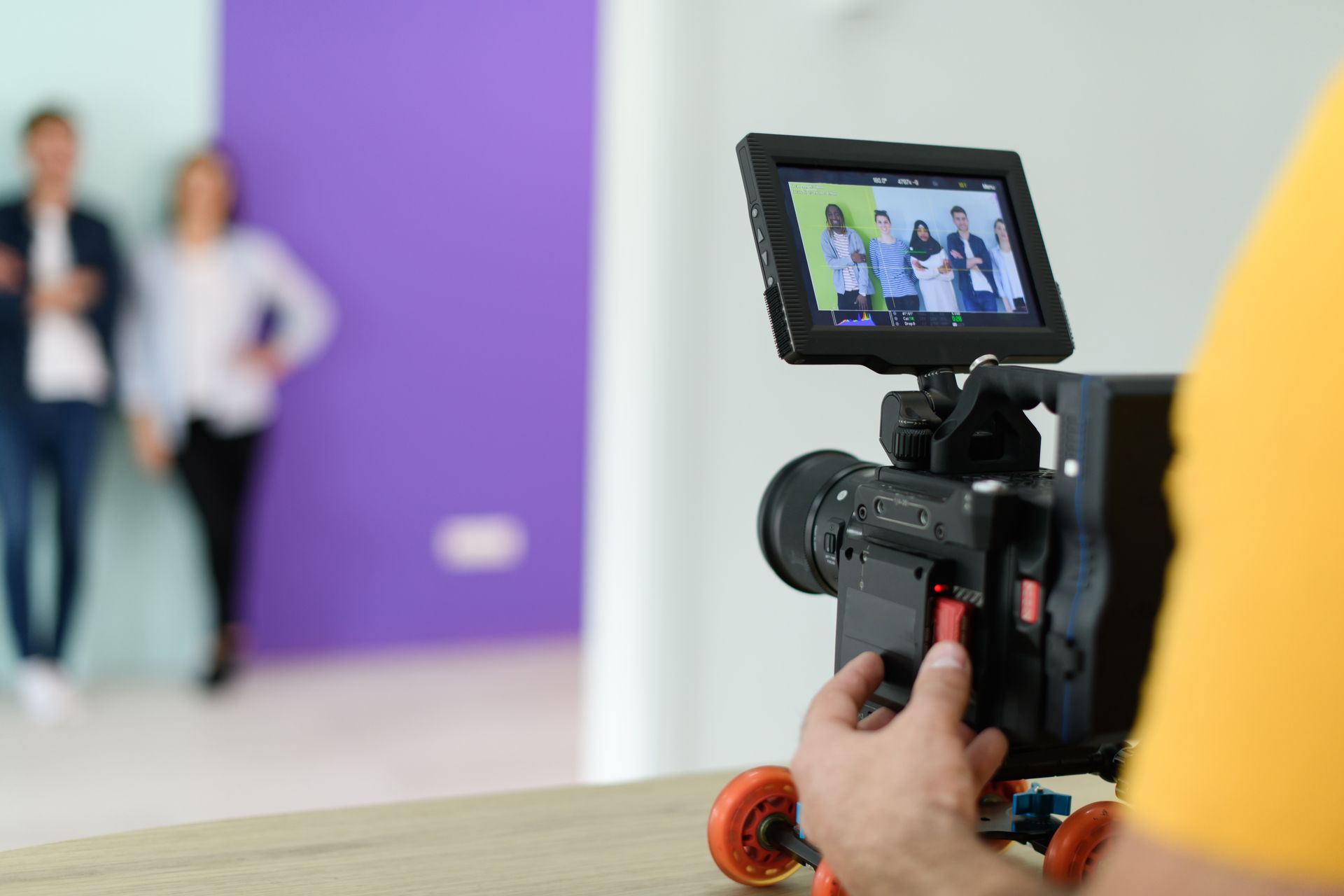 Camera filming two people posing against a purple wall indoors