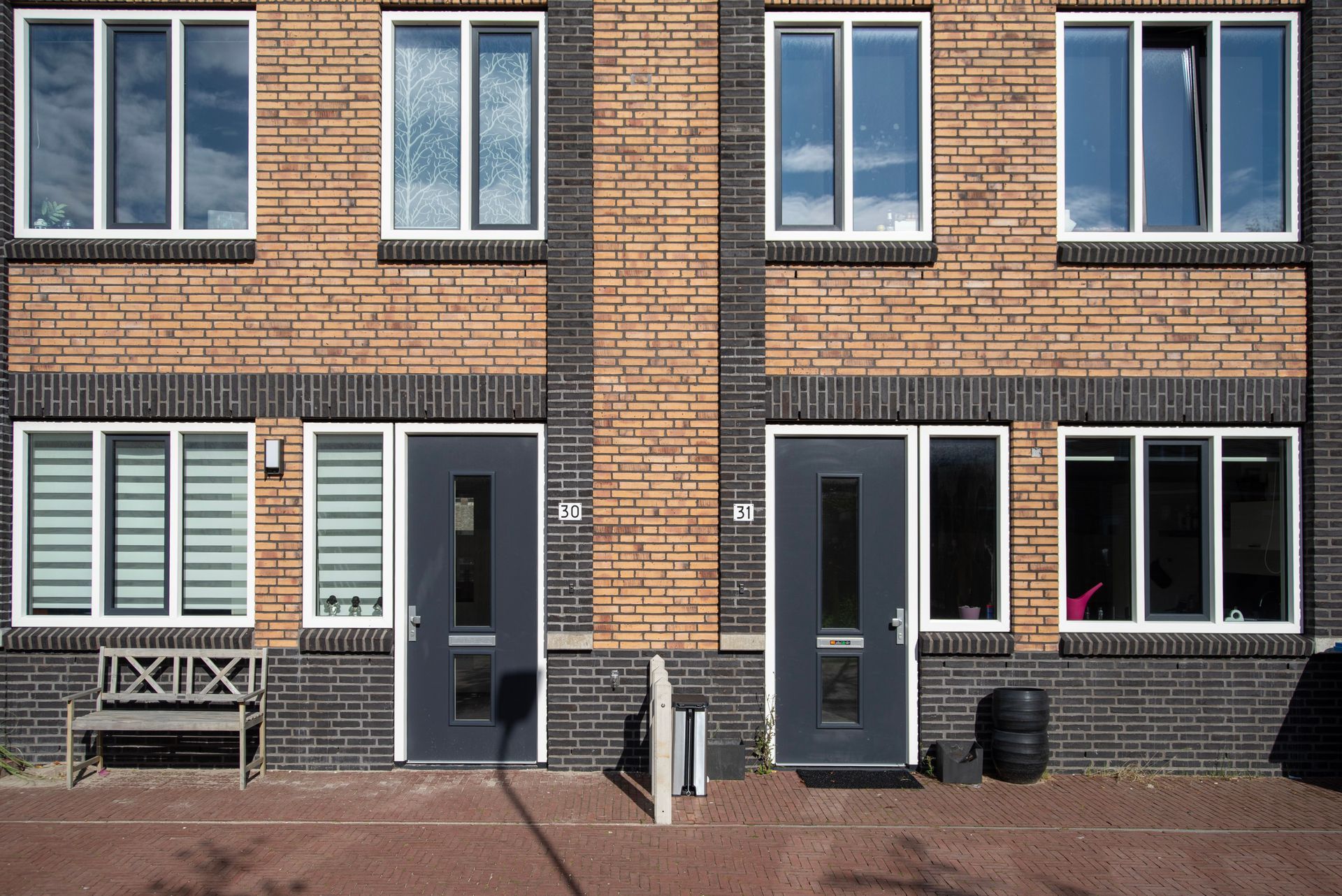 Brick apartment building facade with two front doors, windows, and a paved entrance courtyard