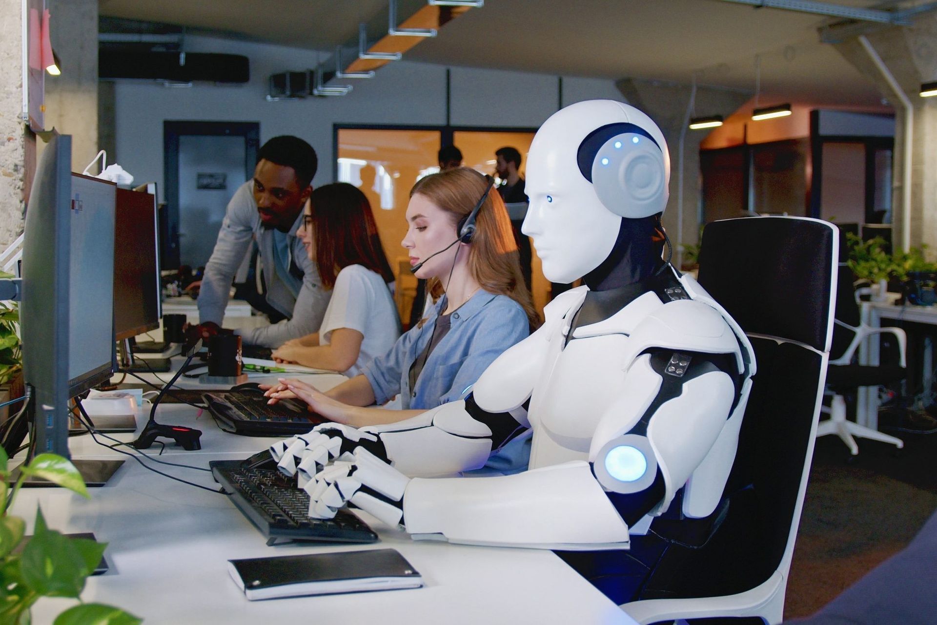 Office workers and a humanoid robot collaborating at a desk in a modern workspace