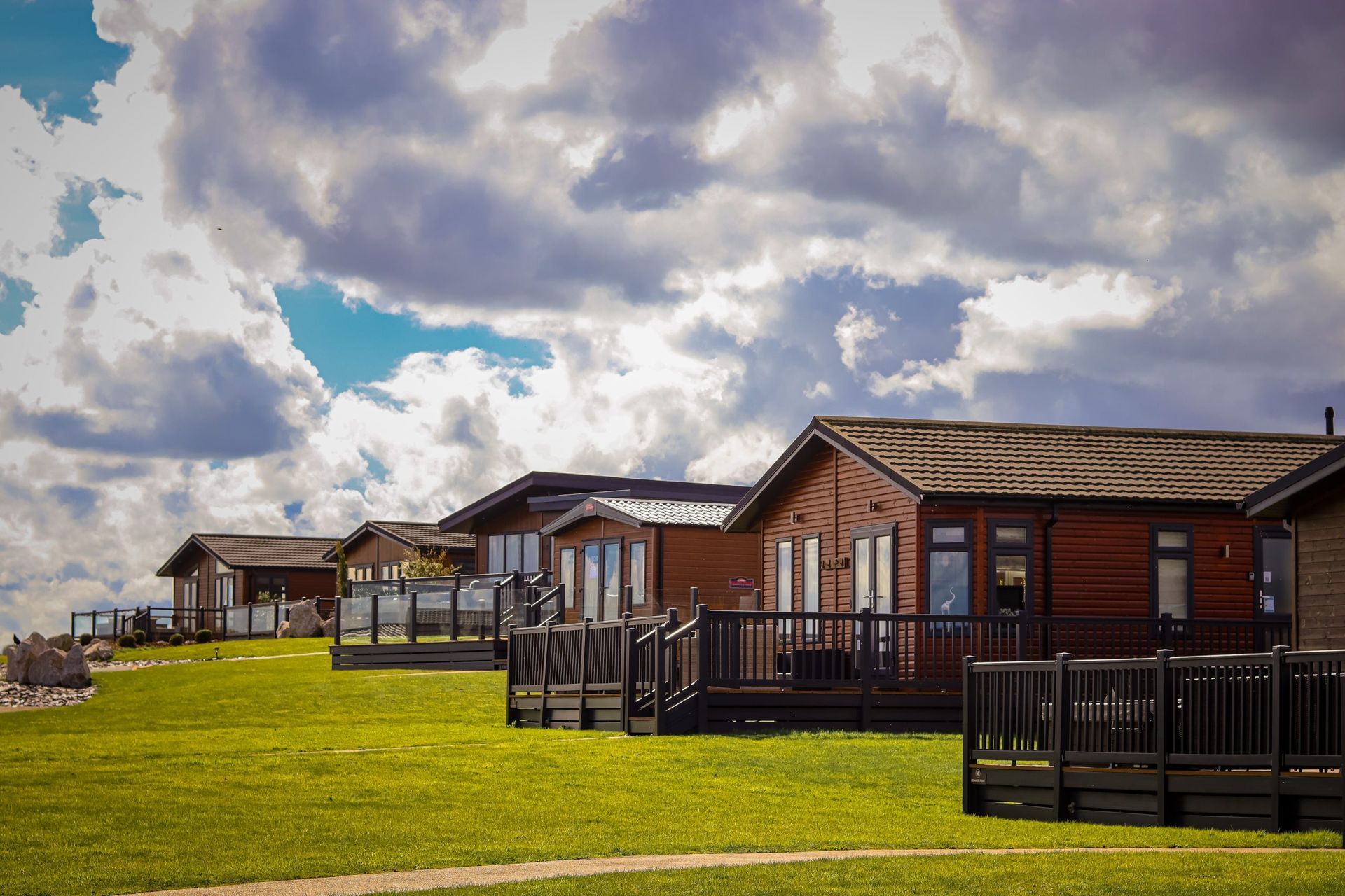 Row of wooden cabins on a grassy hill under a cloudy sky