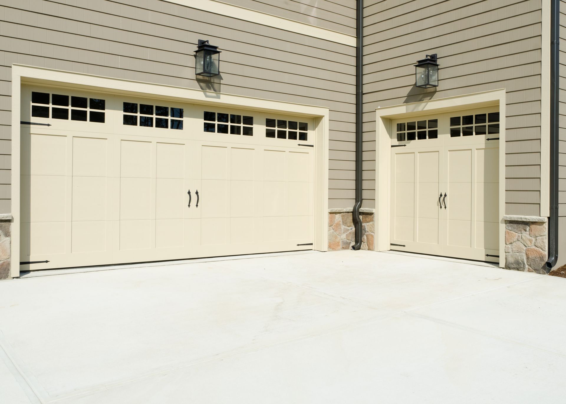 Two beige garage doors with windows, mounted on a tan building, concrete driveway.