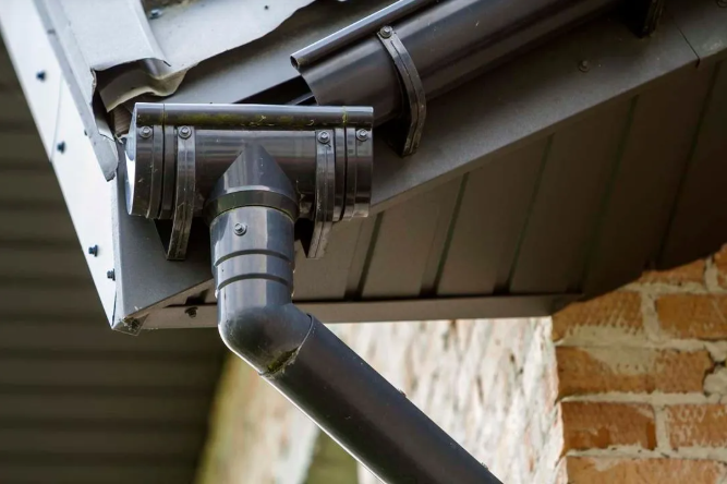 Dark gray gutter system connected to a roof and brick wall.