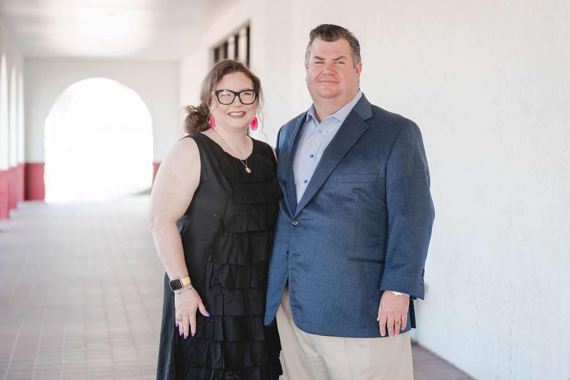 Two people standing in a bright hallway, smiling at the camera.