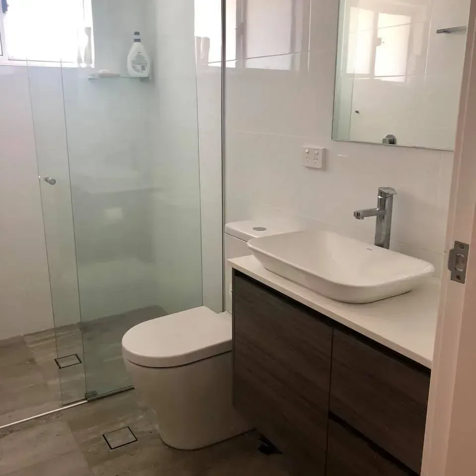 Modern bathroom with glass shower, toilet, floating vanity, and white walls.