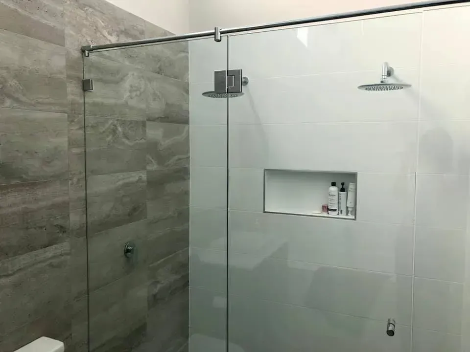 Modern glass shower with gray tiled walls, two showerheads, and built-in shelf.