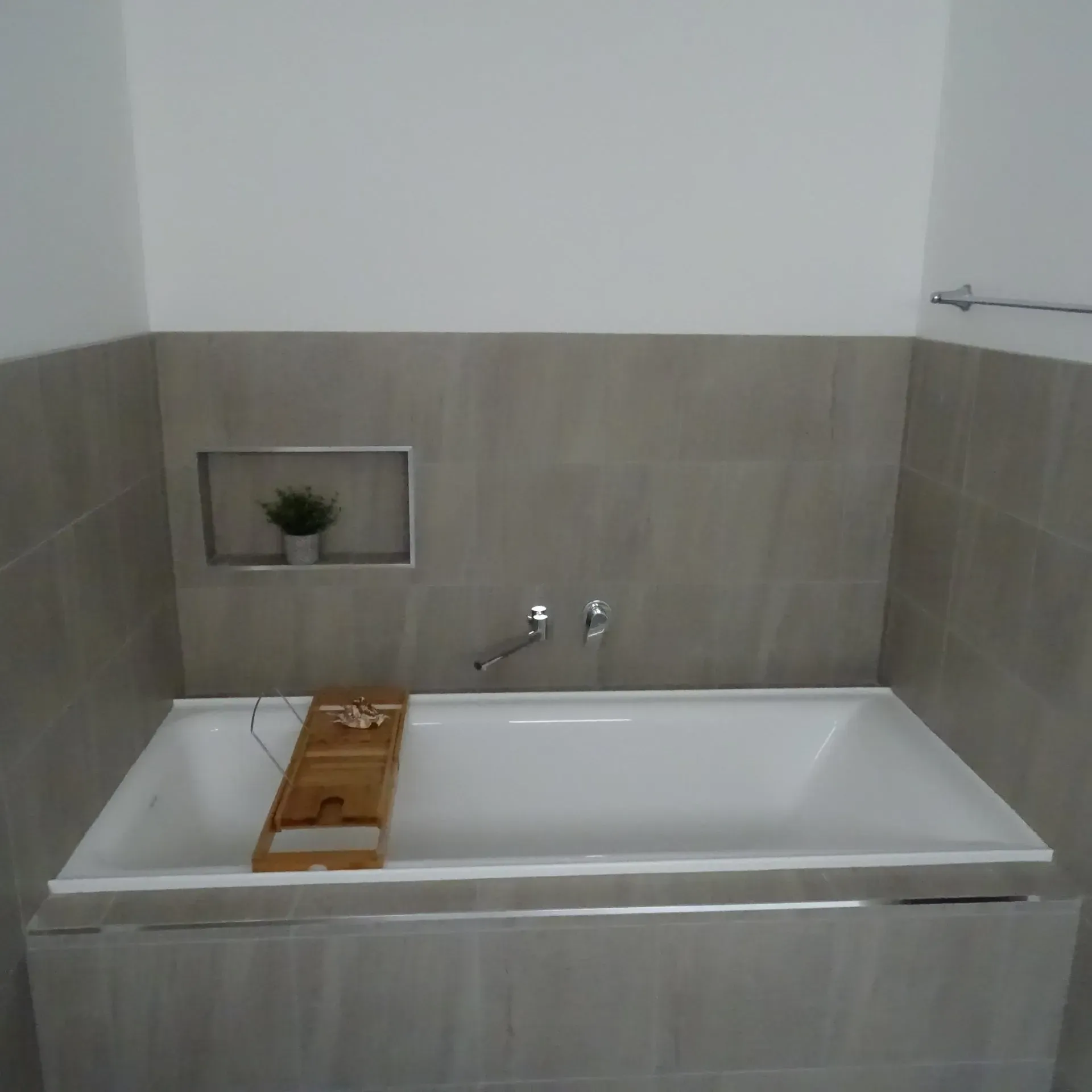 Bathroom with a white bathtub, gray tile wall, and small plant in a recessed niche.