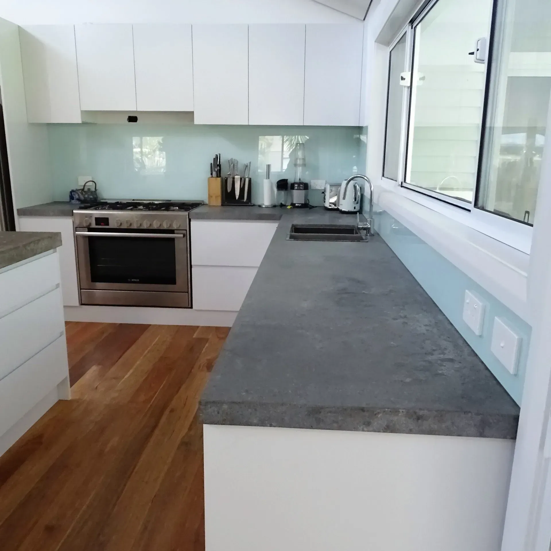 Modern white kitchen with stainless steel appliances, gray countertops, and light blue backsplash.