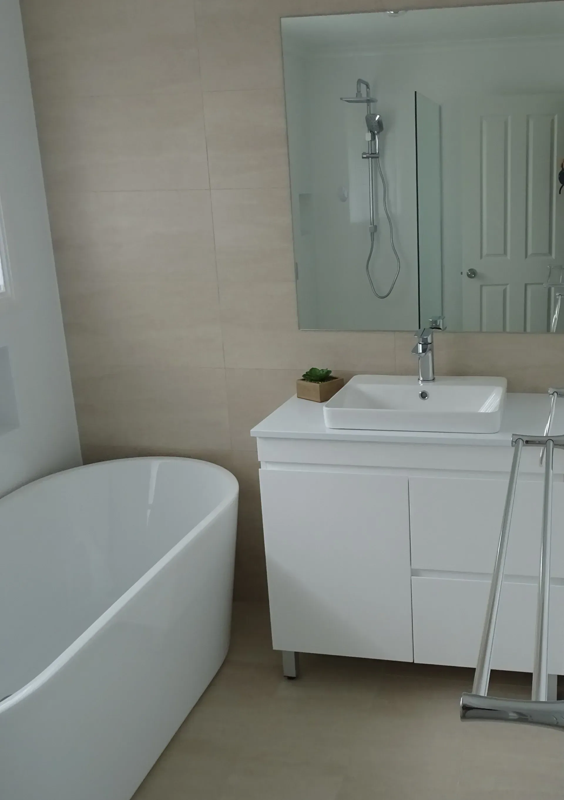 White bathroom with a tub, sink, and mirror. Light beige walls and flooring.