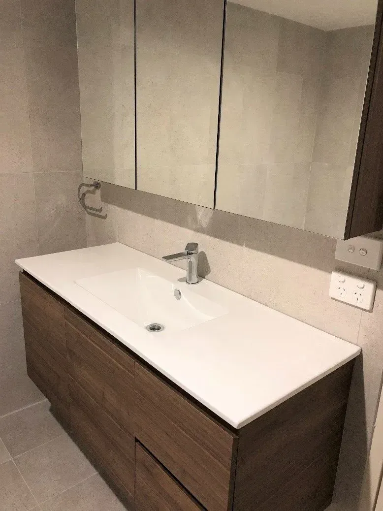 Bathroom vanity with a white sink, wooden cabinet, and large mirror.