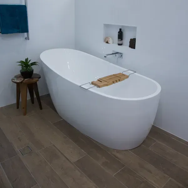 A modern bathroom with a white oval tub, wooden floor, and small side table.