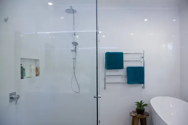 Modern white bathroom with glass shower, teal towels, and a small plant.
