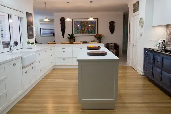 White kitchen with wooden floors, a central island, and various art pieces on the wall.