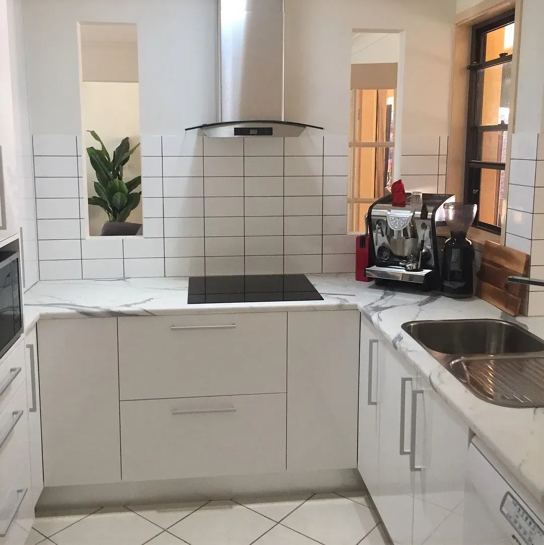 White kitchen with marble countertops, modern appliances, and a window.