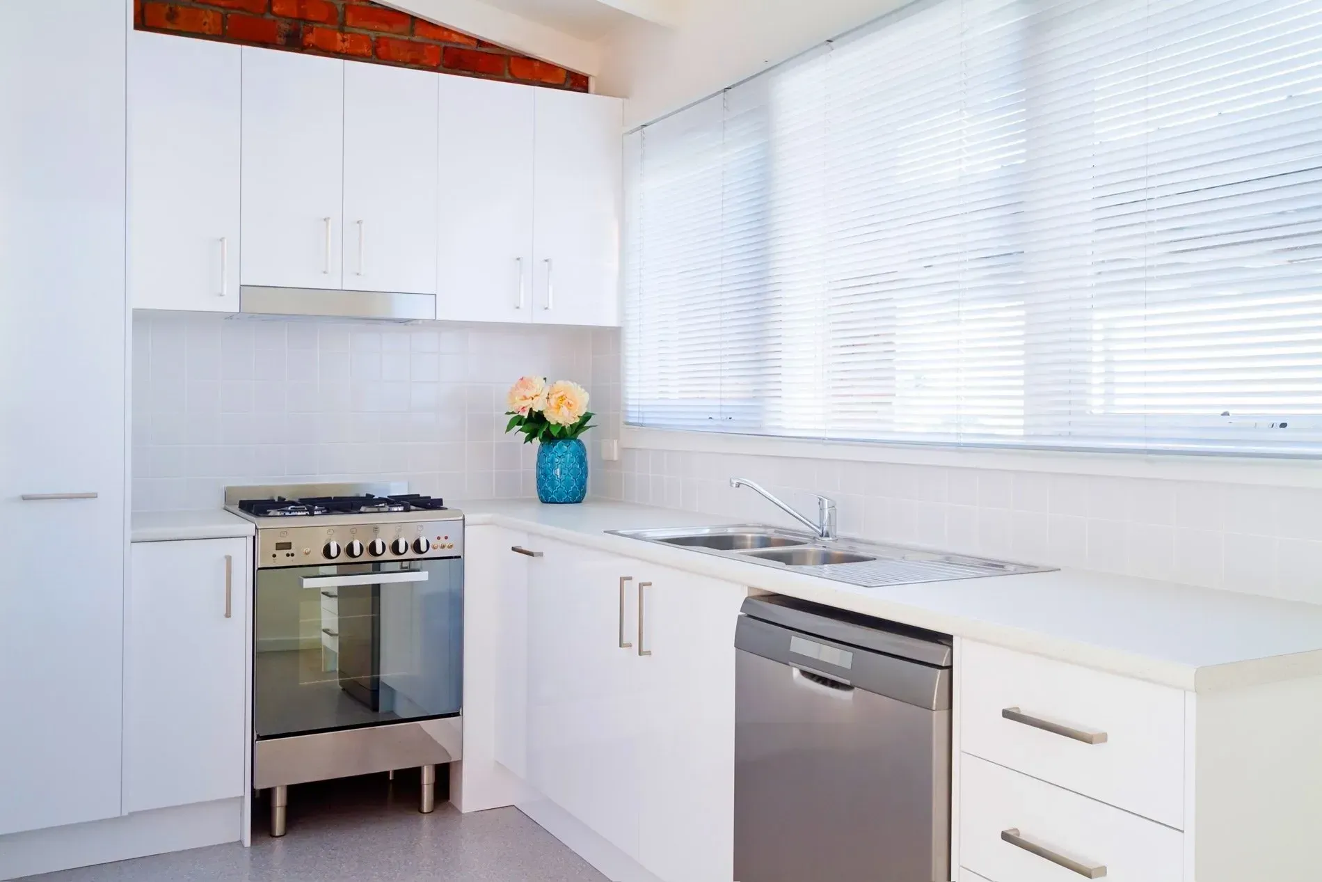 White kitchen with stove, cabinets, sink, and window with blinds.