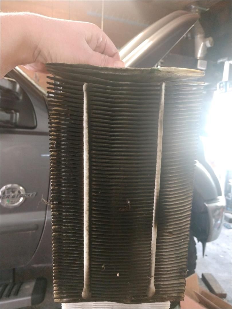 A person is holding an air filter in front of a car. |