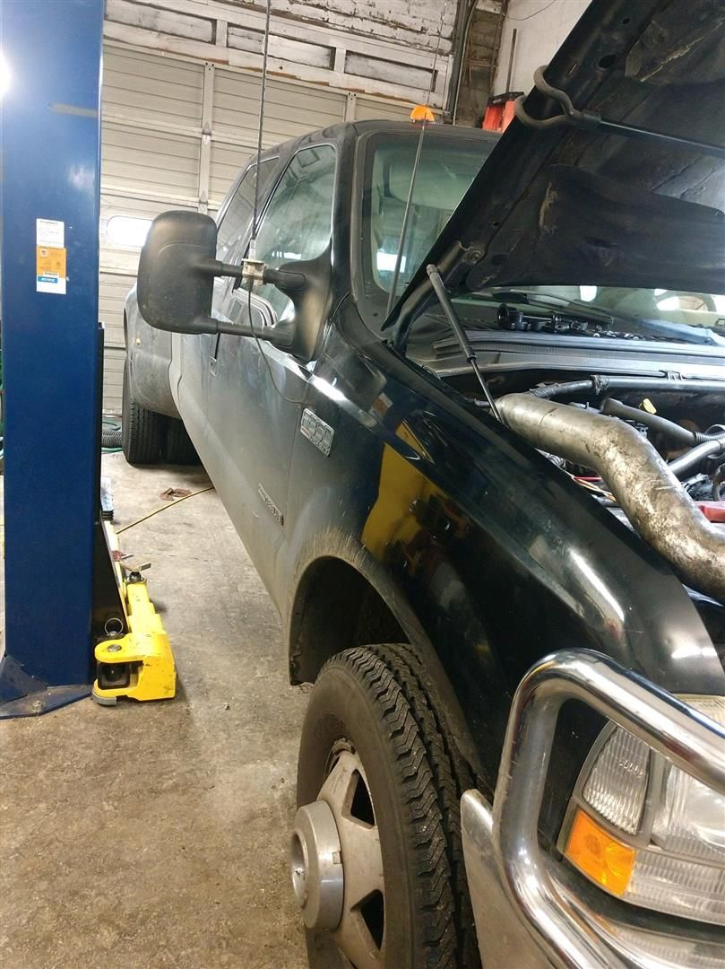 A black truck with the hood up is on a lift in a garage. | J&H Automotive