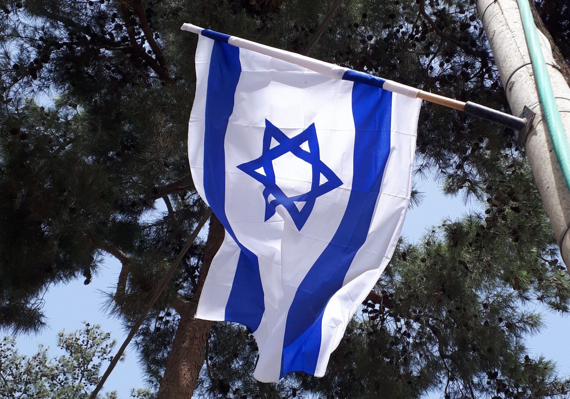 Israeli flag waving in the wind, blue and white with a Star of David, outdoors.