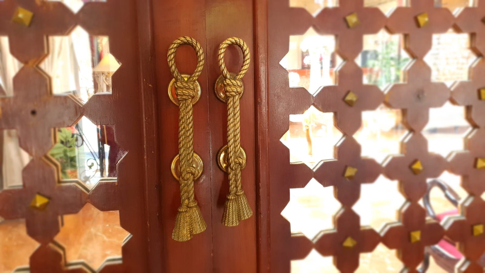 Ornate, carved wooden door with gold rope-style handles. The door has a latticework design with gold accents.