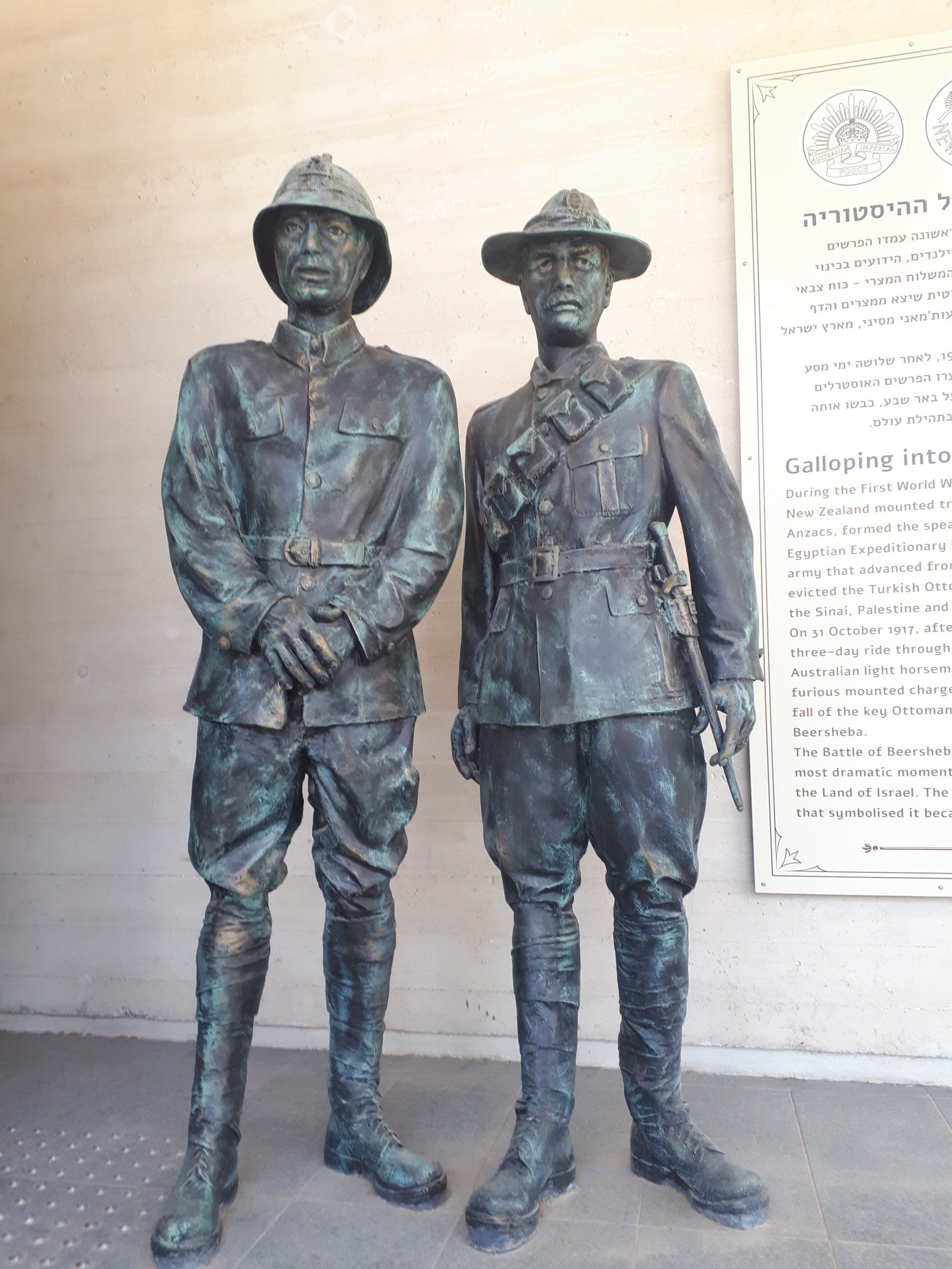 Two bronze statues of men in military uniforms, standing in front of a wall with text.