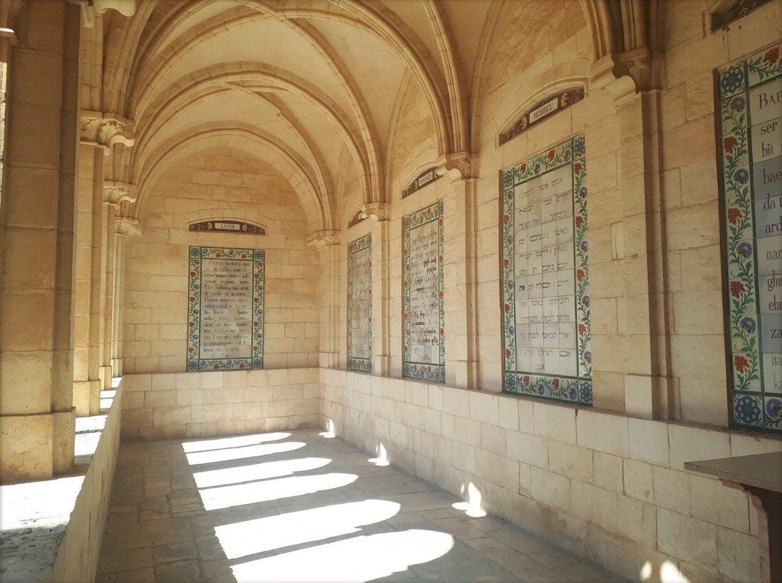 Stone corridor with arched ceiling and tiled panels, lit by sunlight.