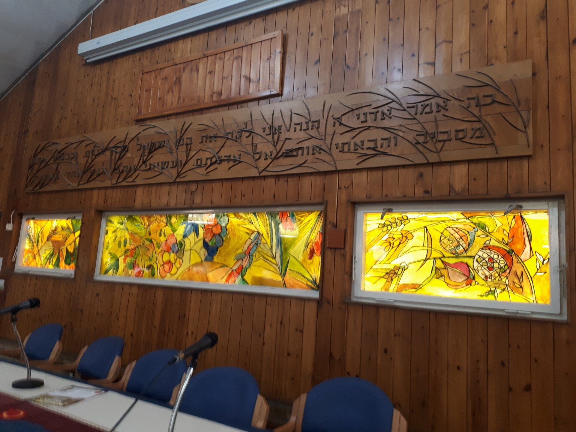 Wooden wall with stained glass windows and Hebrew script.