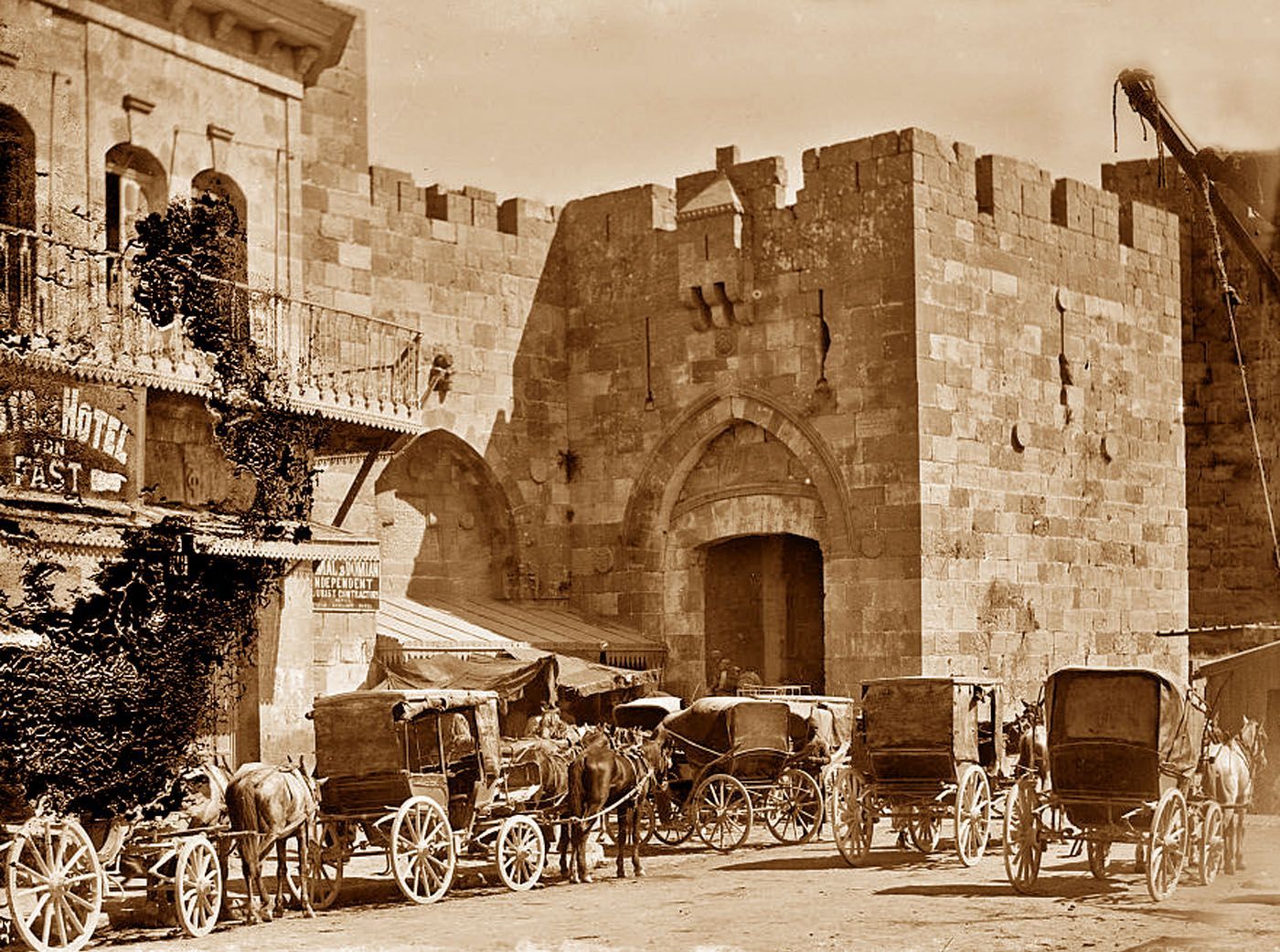 Old photo: Horse-drawn carriages lined up near the gate of a stone walled city.
