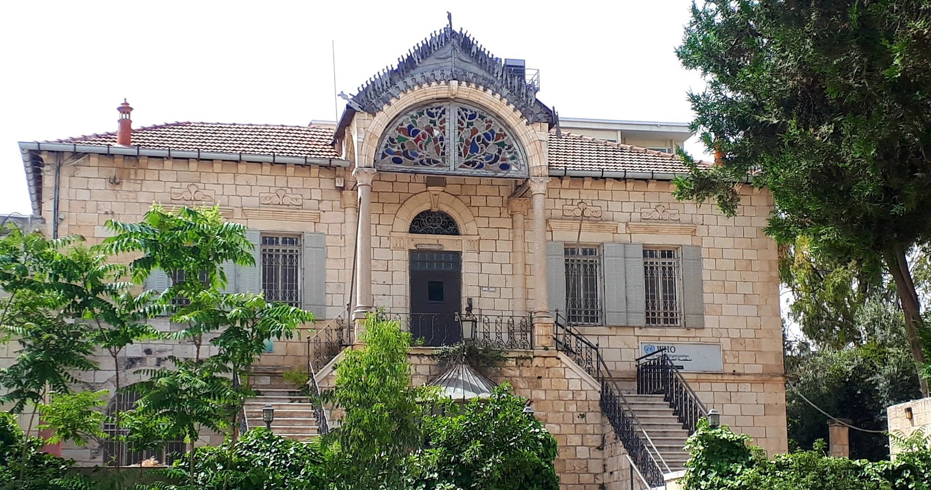 Stone building with arched window detail, steps leading up to the front entrance. Trees in front.