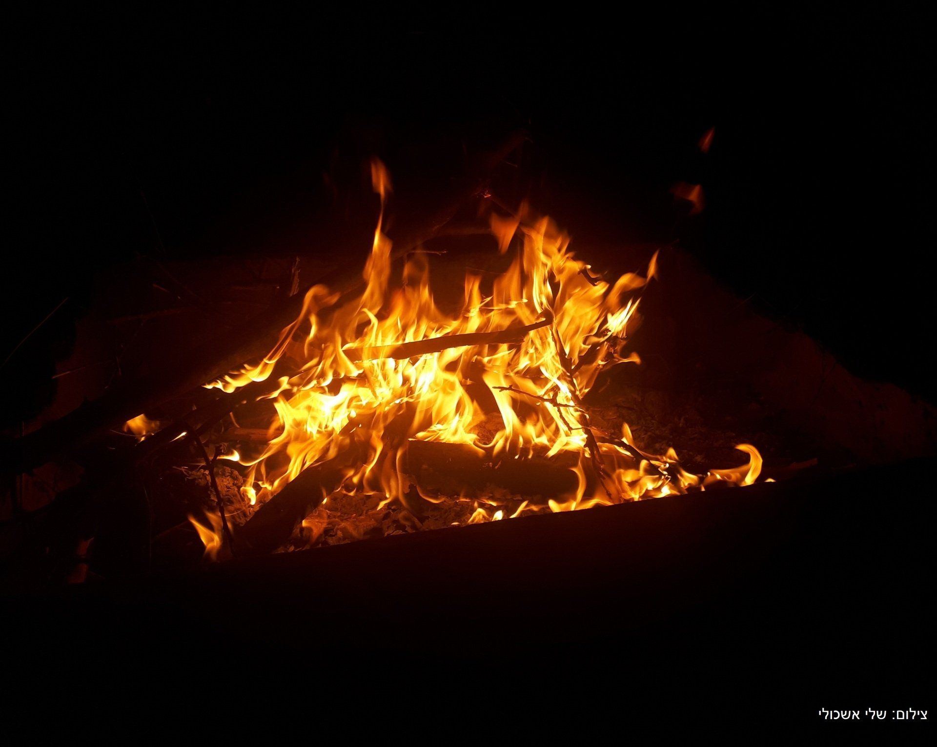 Bonfire burning brightly at night, with flames and glowing embers.