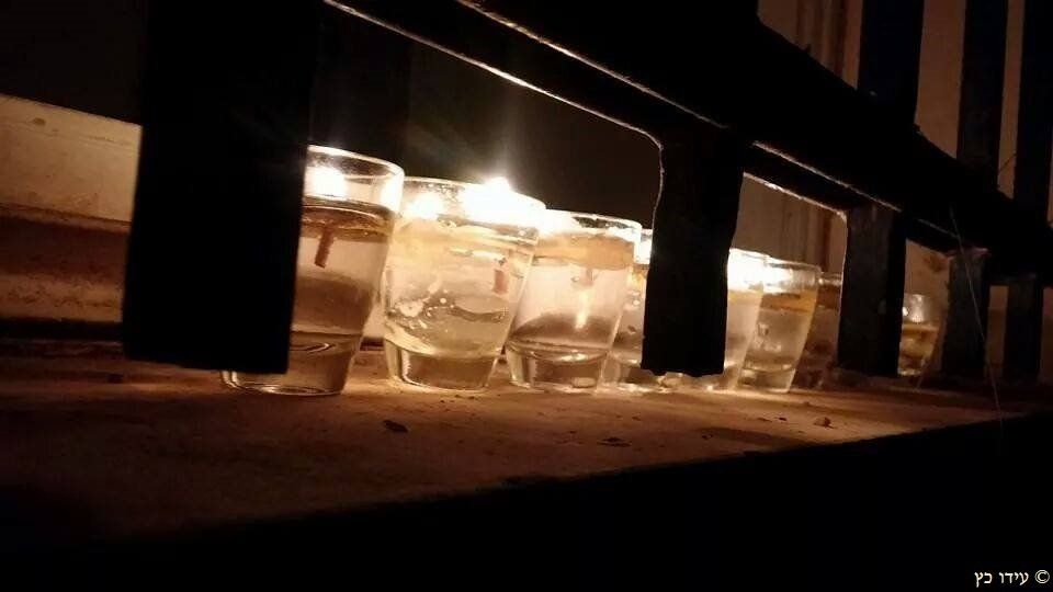 Candlelit glasses of water on a ledge, viewed from below a black railing.