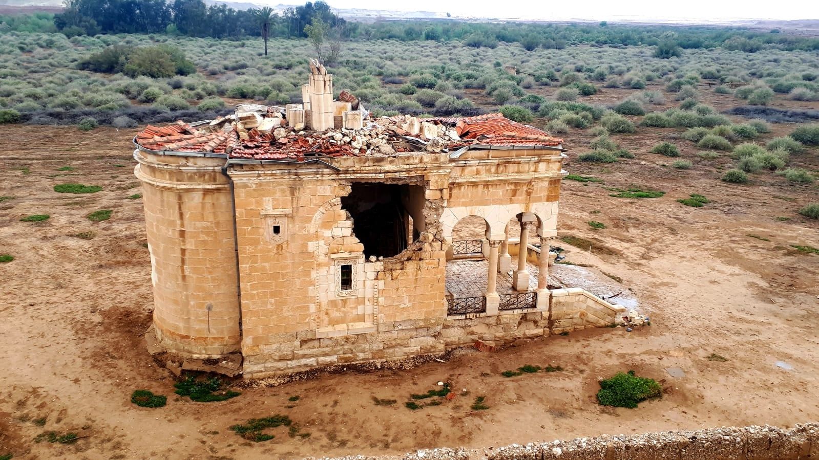 Ruined church building in a dried lakebed; tan stone with damaged roof and walls.