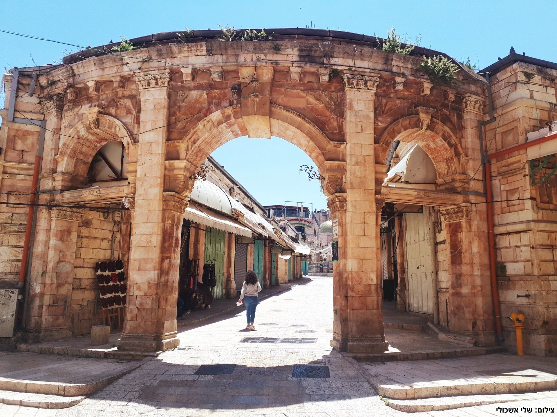 Stone archway in Jerusalem with a person walking down a narrow street. Bright sunny day.