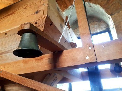 Bronze bell hanging from a wooden beam inside a building with an arched opening.