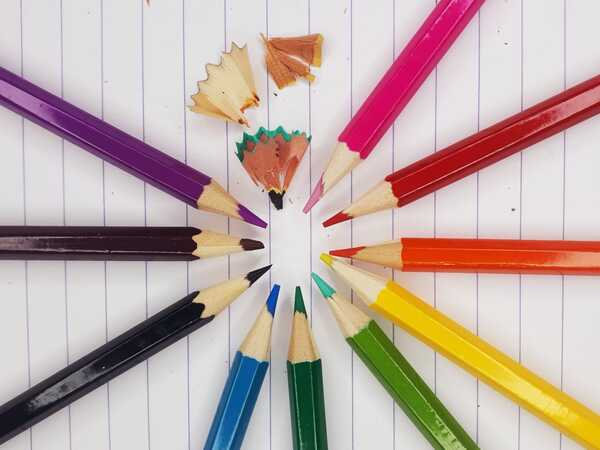 Colored pencils arranged in a circle, with shavings, on lined paper.
