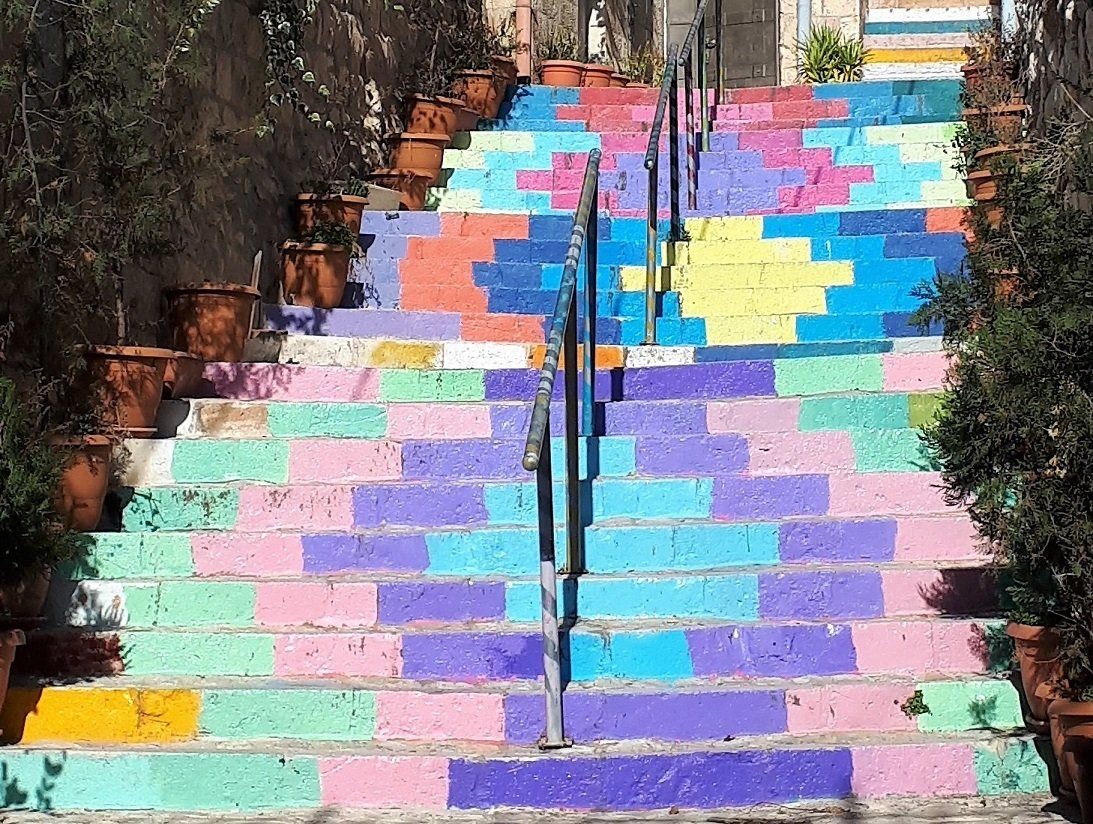Colorful painted steps with brick-like patterns, flanked by plants in pots and a central metal railing.