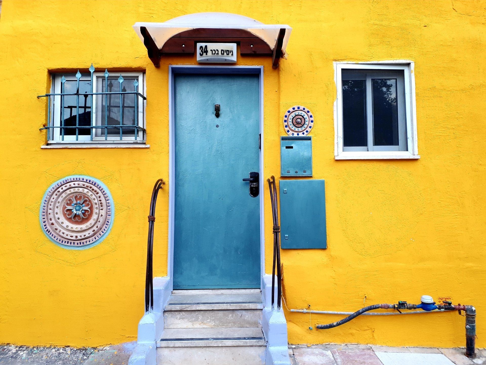 Yellow building with a blue door, two windows, and colorful tile decorations.