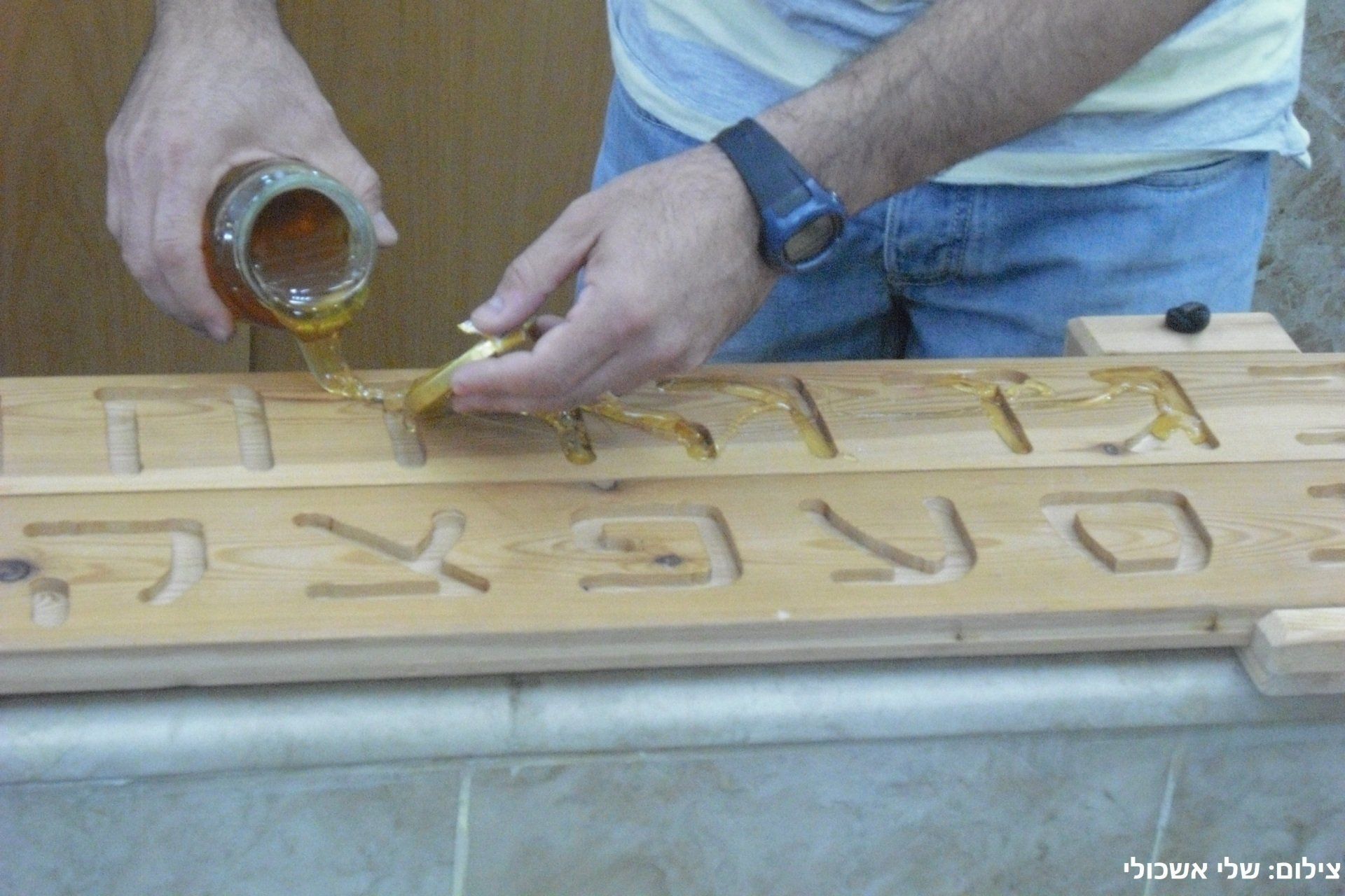 Person pouring honey onto wooden board with Hebrew letters.