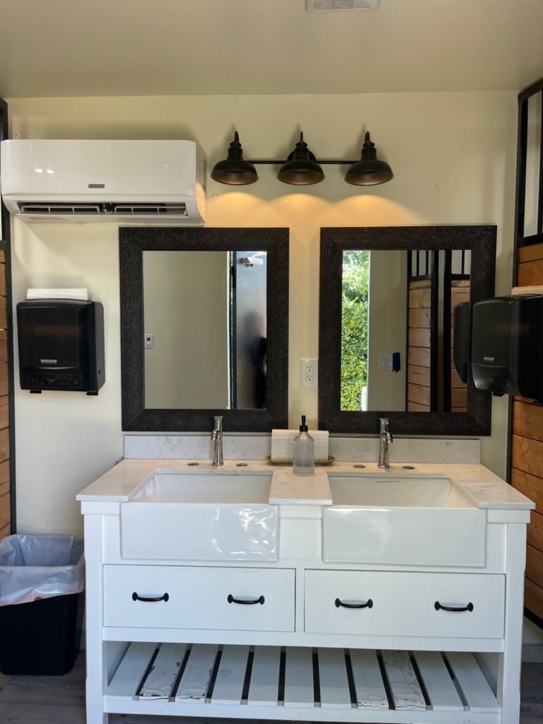 Modern bathroom vanity with double sinks, mirrors, wall lights, and air conditioner above