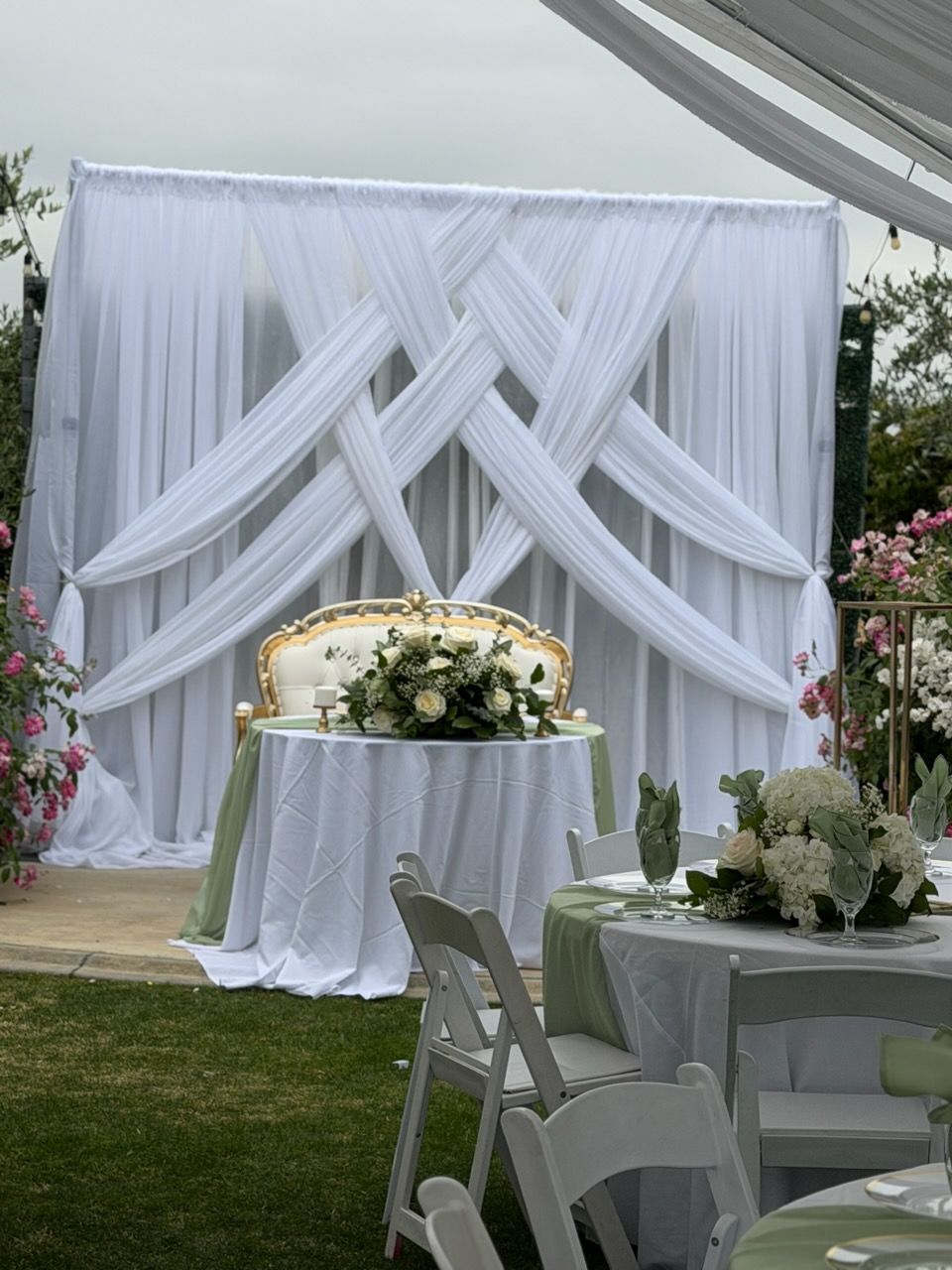 White draped wedding altar with floral table centerpiece and chairs on a lawn outdoors
