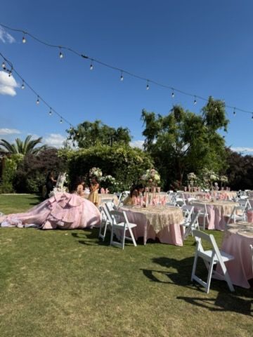 Outdoor garden party with pink table settings, white chairs, string lights, and a large pink balloon display