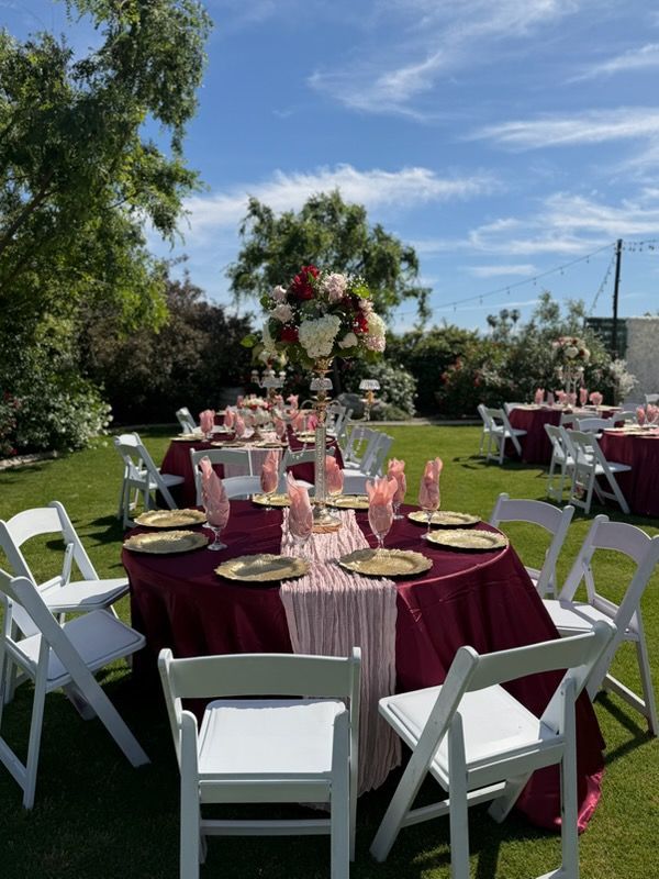 Outdoor wedding reception with round tables, maroon tablecloths, pink decor, and white chairs on a lawn