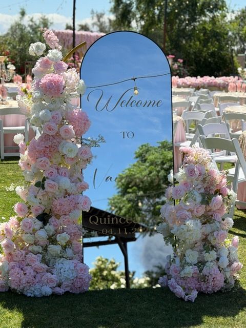 Floral wedding sign with pastel pink and white flowers and a blue welcome mirror on a lawn