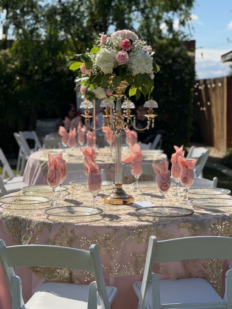 Decorated outdoor round table with pink napkins, glassware, and a floral centerpiece at a garden party
