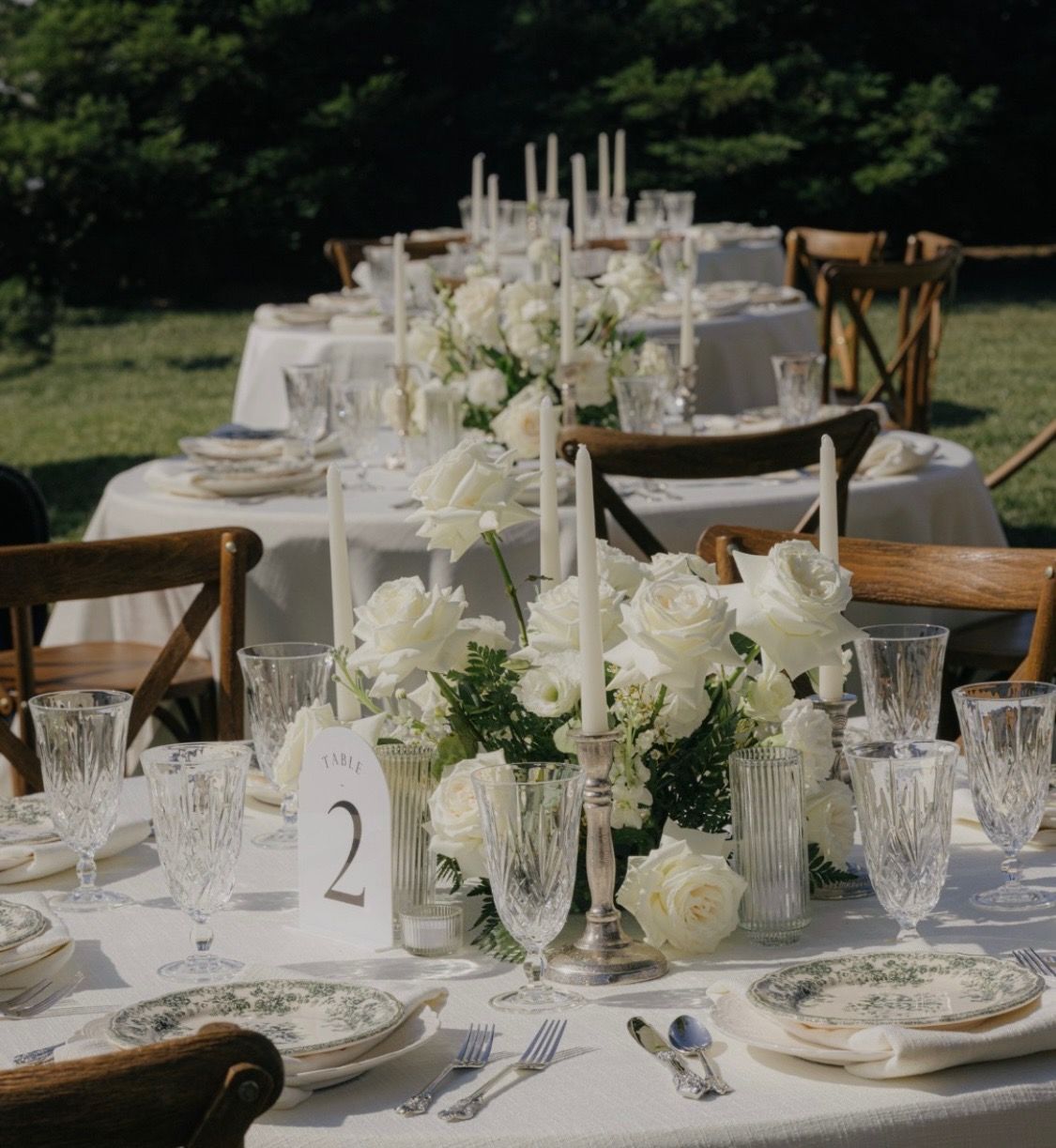 Elegant outdoor wedding reception tables set with white flowers, candles, and glassware on a lawn