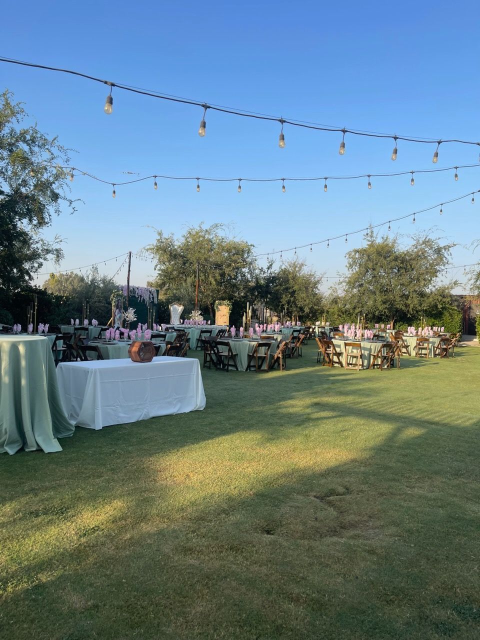 Outdoor reception on a lawn with string lights, tables, and guests at sunset
