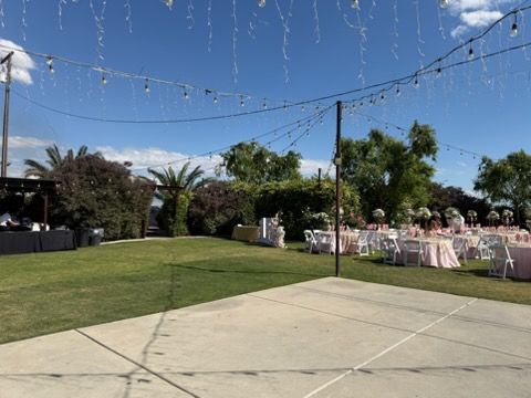 Outdoor event lawn with string lights, white tables and chairs, and a blue sky