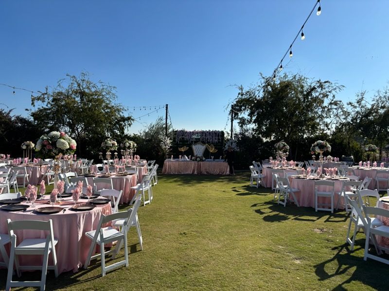 Outdoor wedding reception setup with pink table settings on a grassy lawn under blue sky