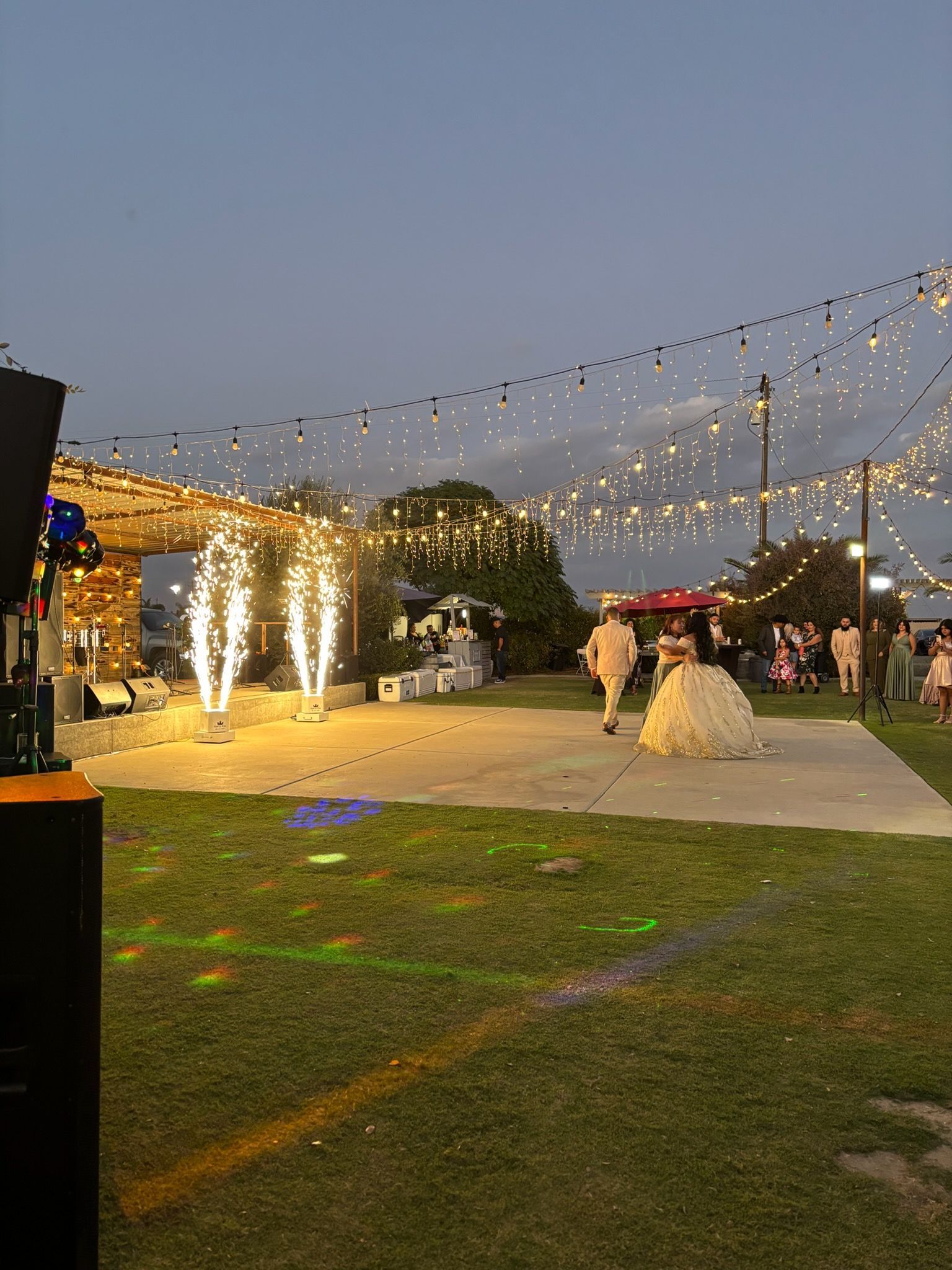 Outdoor evening wedding reception with string lights, glowing decorations, and a white dress on the lawn