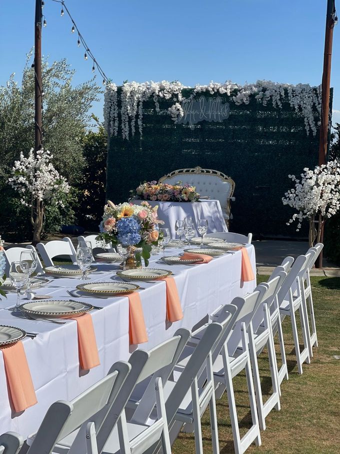 Picnic tables set outdoors with floral centerpieces, prepared for a celebration at sunset.