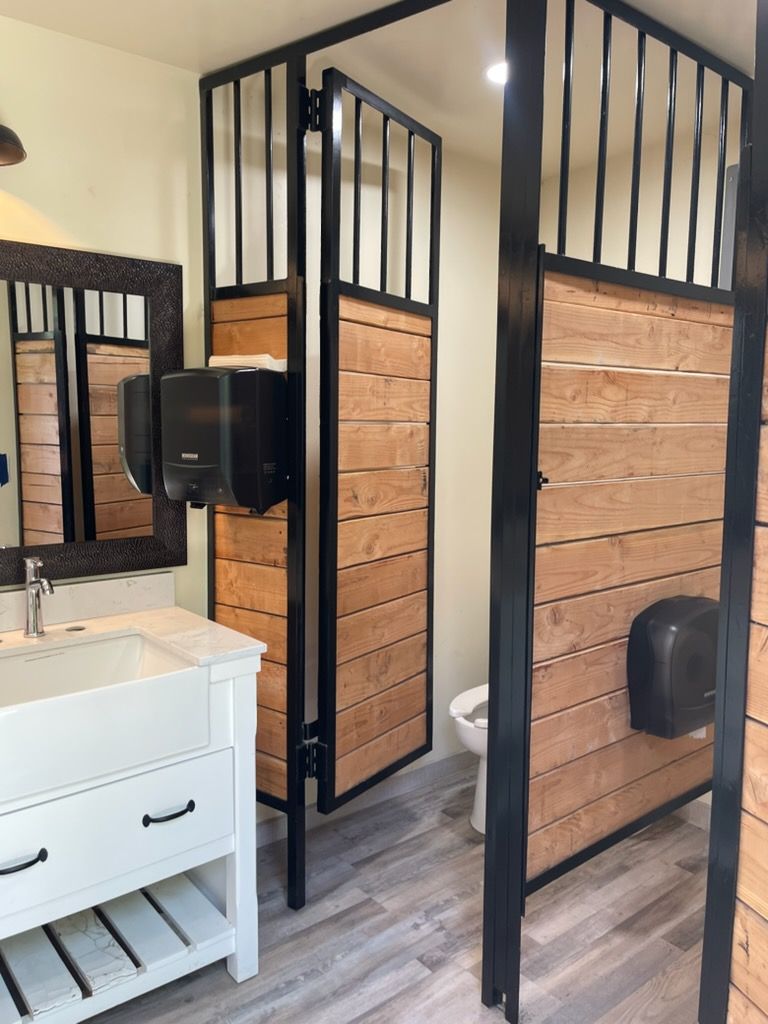 Bathroom with two black-framed wooden shower stalls beside a white sink and mirror