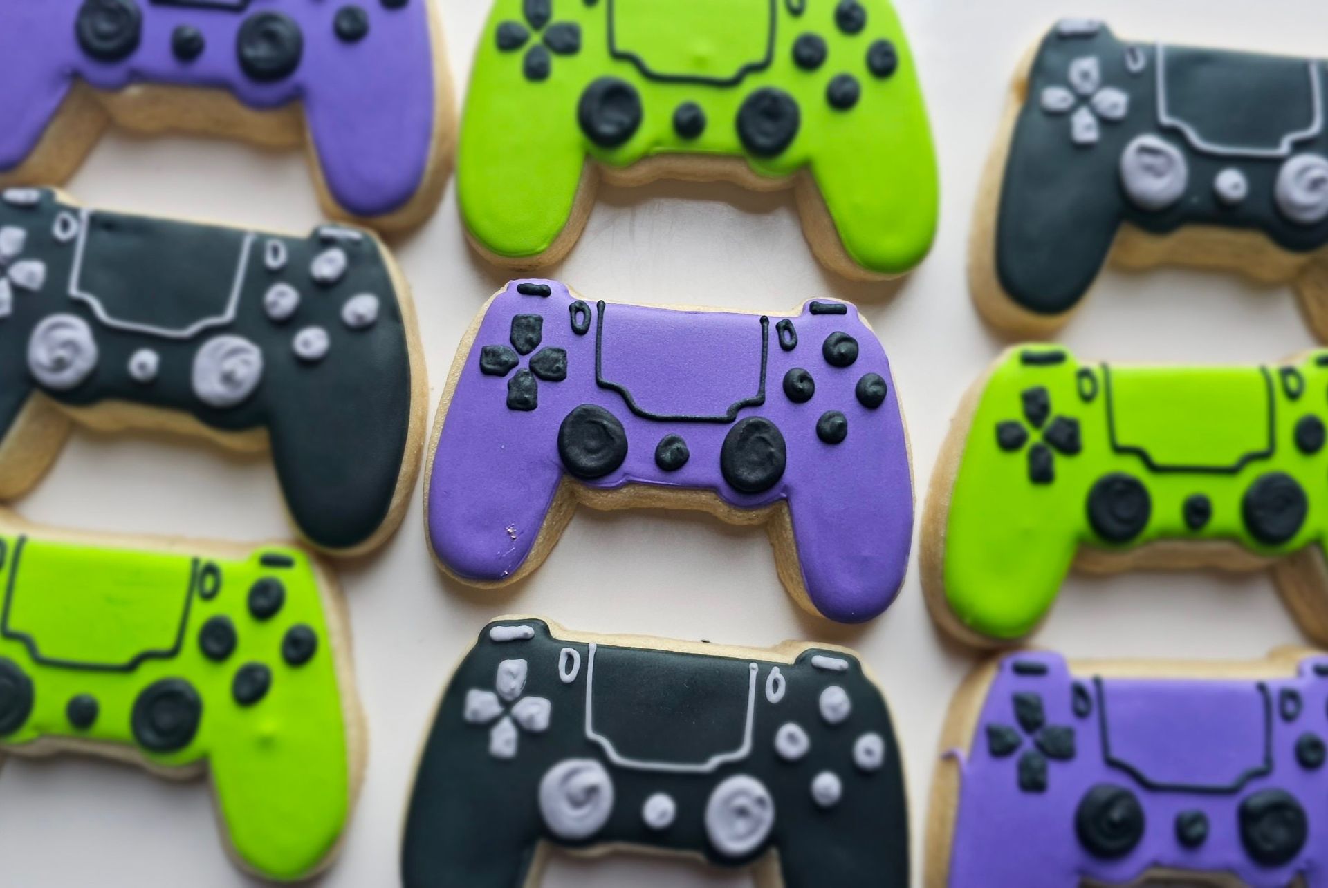 Multiple controller-shaped sugar cookies in black, bright green, and purple arranged on a white surface.